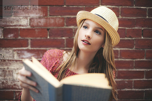 Mädchen liest Buch in der Nähe von Ziegelmauer