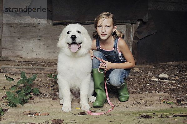 Mädchen hockt mit Hund in baufälligem Schuppen
