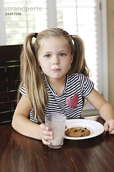 Mädchen isst Kekse mit Milchschnurrbart am Tisch