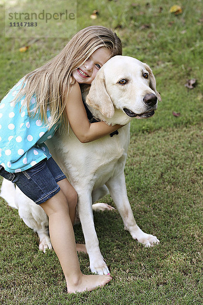 Lächelndes Mädchen umarmt Hund im Feld