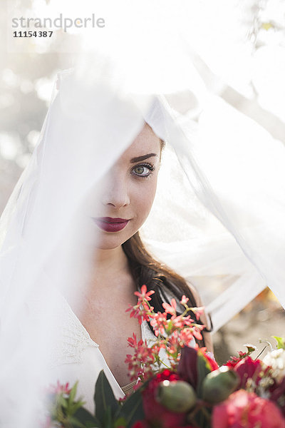Kaukasische Braut hält Blumenstrauß unter Schleier