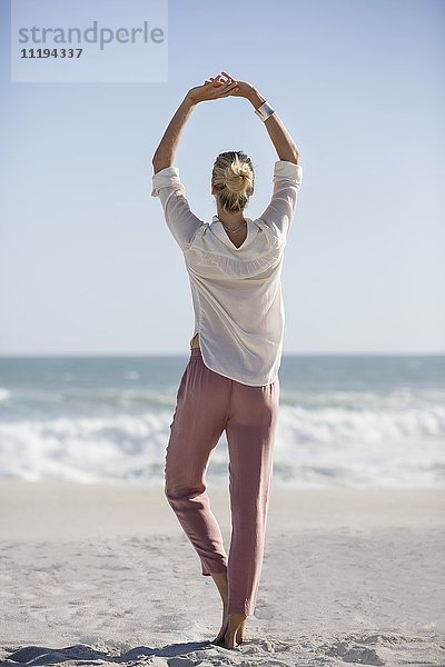 Schöne junge Frau beim Yoga am sonnigen Strand