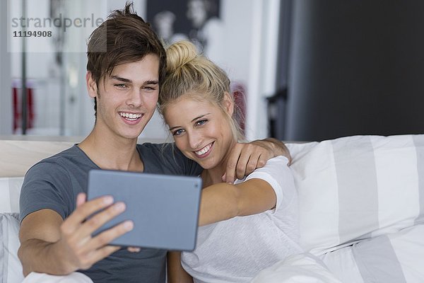Ein junges Paar,  das einen Selfie auf dem Bett nimmt.