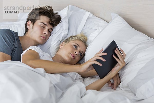 Junge Frau,  die ein digitales Tablett benutzt,  während ihr Freund in ihrer Nähe schläft.