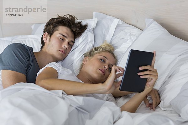 Junge Frau,  die ein digitales Tablett benutzt,  während ihr Freund in ihrer Nähe schläft.