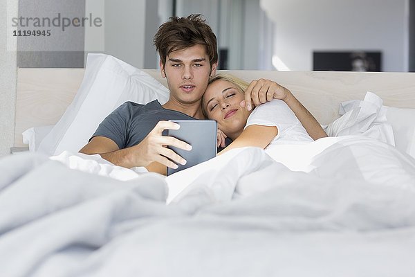 Ein Paar sieht sich einen Film auf einem digitalen Tablett auf dem Bett an.