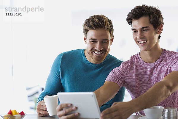 Nahaufnahme von zwei glücklichen jungen Männern,  die Selfie mit einem digitalen Tablett nehmen.
