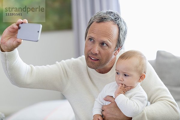 Glücklicher Vater mit seiner kleinen Tochter,  die Selfie mit Fotohandy nimmt.
