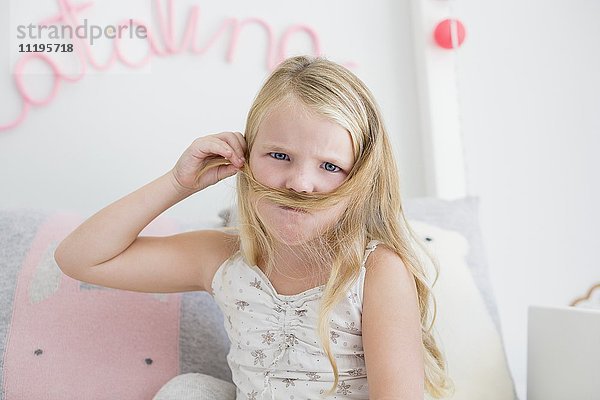 Porträt eines kleinen Mädchens,  das mit seinen Haaren Schnurrbart macht.