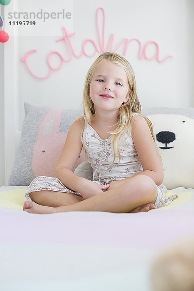 Porträt eines glücklichen kleinen Mädchens,  das auf dem Bett sitzt