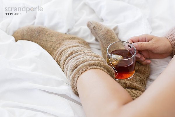 Nahaufnahme einer Frau mit einer Tasse Kräutertee im Bett