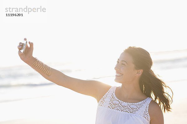 Schöne junge Frau,  die Selfie mit Smartphone am Strand nimmt