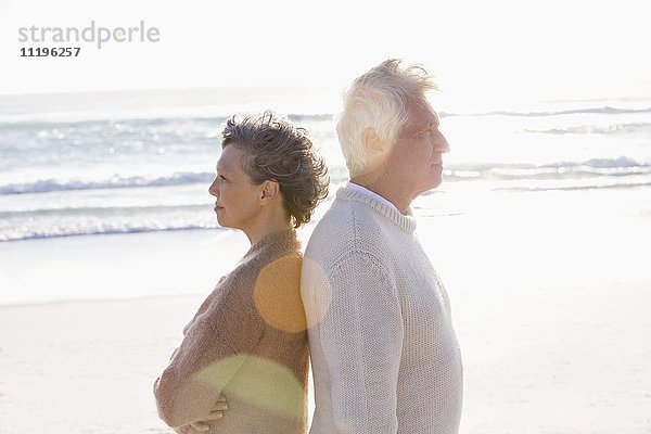Altes Paar steht Rücken an Rücken am Strand