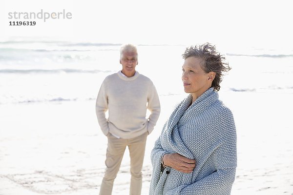 Frau am Strand stehend mit ihrem Mann im Hintergrund