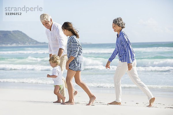 Altes Paar,  das mit seinen Enkelkindern am Strand spazieren geht.