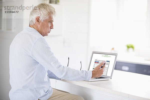 Senior Mann mit Handy und Laptop in der Küche