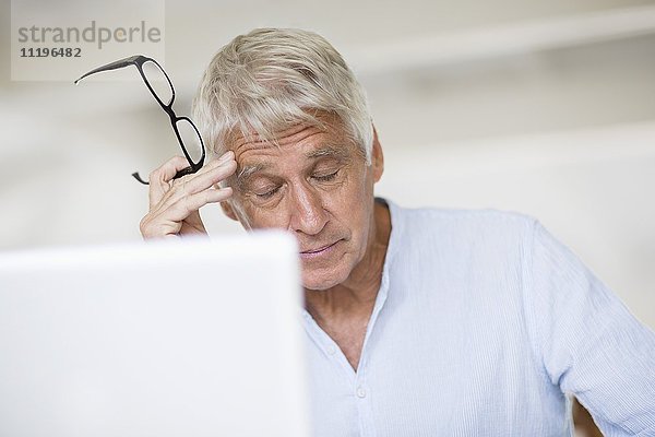 Müde Senior Mann Kopf in Hand mit Laptop auf dem Tisch