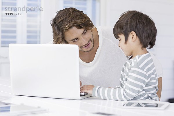 Vater im Gespräch mit dem Sohn bei der Benutzung des Laptops zu Hause