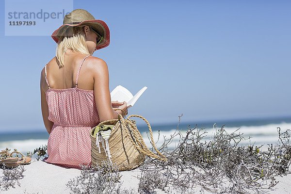 Schöne Frau,  die ein Buch am Strand liest.