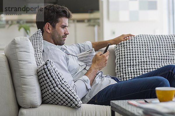 Mann,  der auf einer Couch sitzt und ein Smartphone benutzt.