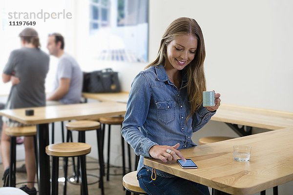 Glückliche Frau trinkt Kaffee und benutzt ein Smartphone in einem Restaurant.