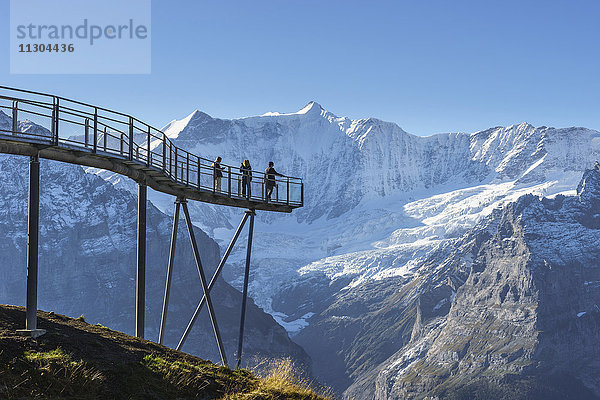 Gipfelweg und Aussichtsplattform mit dem Namen First Cliff Walk auf dem Gipfel des First oberhalb von Grindelwald,  Berner Oberland,  Schweiz. Im Hintergrund die Berge Kleines Fiescherhorn (links) und Grosses Fiescherhorn.