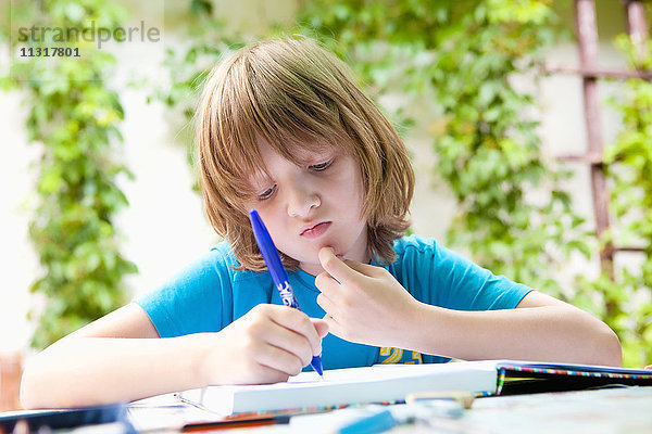 Junge mit blondem Haar bei den Hausaufgaben im Freien