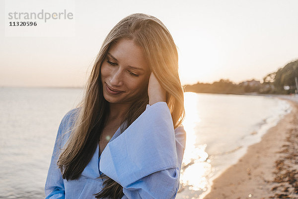 lächelnde junge Frau am Strand bei Sonnenuntergang