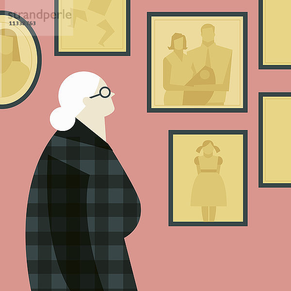 Alte Dame schaut auf Familienfotos an der Wand