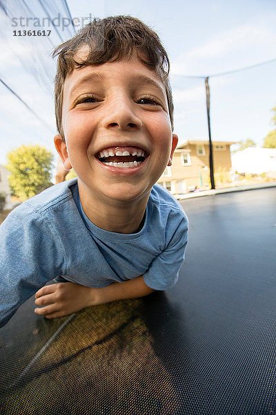 Porträt eines Jungen,  der sich auf einem großen Trampolin abstützt und lacht