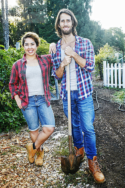 Porträt eines Paares,  das mit einer Schaufel im Garten posiert