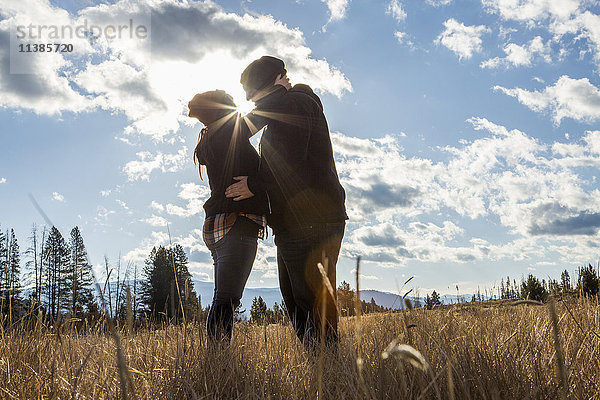 Kaukasisches Paar küsst sich in einem sonnigen Feld