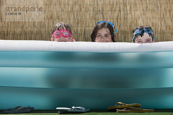 Lächelnde kaukasische Kinder,  die sich in einem aufblasbaren Schwimmbecken verstecken