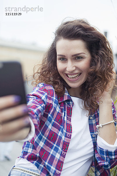 Junge Frau,  die ein Smartphone benutzt,  um einen Selfie zu nehmen.