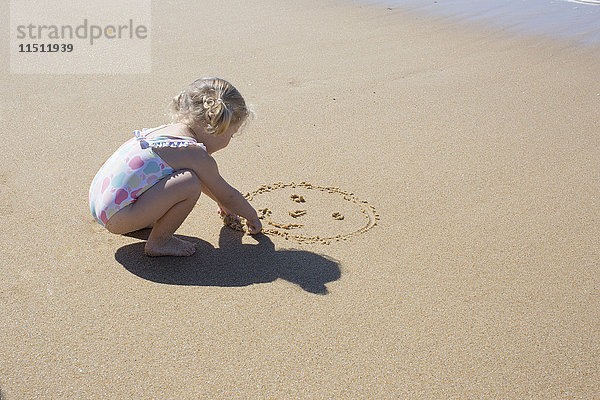 Kleines Mädchen zeichnet Smiley-Gesicht in Sand