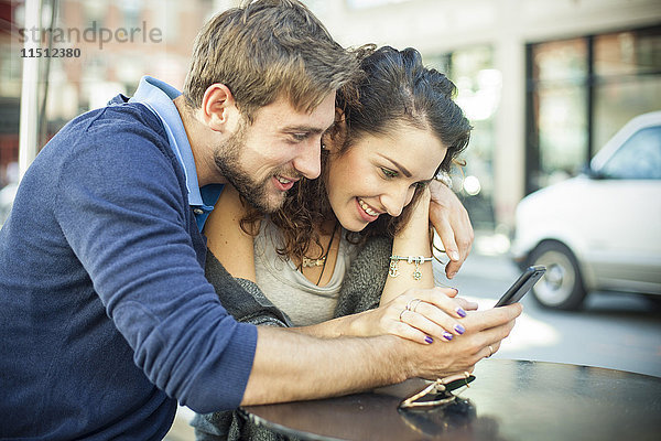 Paar sitzt zusammen im Freien und schaut auf das Smartphone
