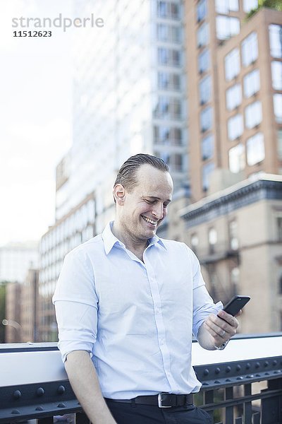 Mann lacht,  während er sein Smartphone im Freien benutzt.