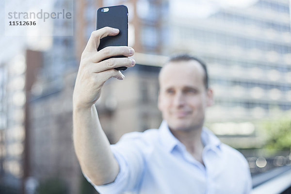 Mann,  der ein Smartphone benutzt,  um einen Selfie zu nehmen.