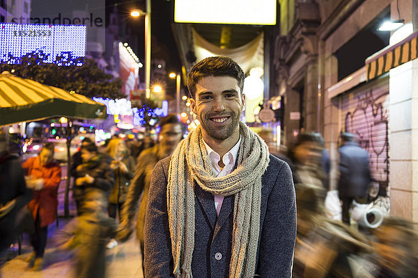 Porträt eines lächelnden Mannes in der Stadt mit unkonzentrierten Menschen bei Nacht