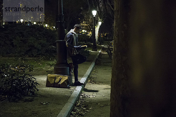 Mann liest ein Buch in einem Park bei Nacht.