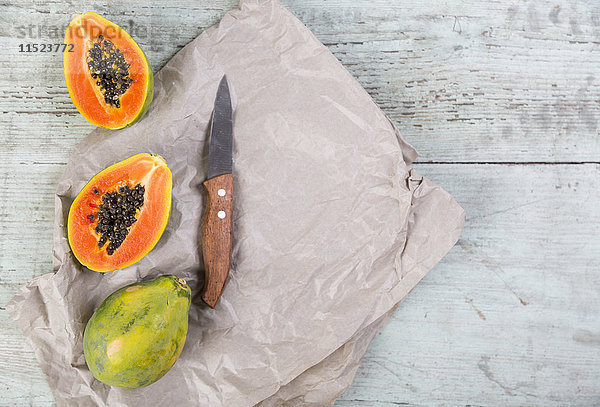 Ganze und geschnittene Papaya und ein Küchenmesser auf Papier und Holz