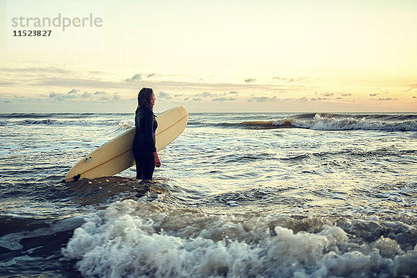Junge Frau mit Surfbrett bei Sonnenuntergang