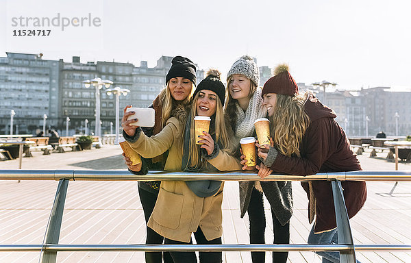 Vier Freunde mit Kaffee zum Mitnehmen eines Selfie mit Smartphone