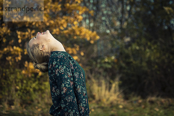 Blonde junge Frau stehend mit Kopf zurück im Herbstwald