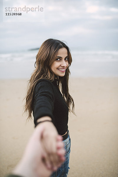 Porträt einer glücklichen jungen Frau,  die am Strand die Hand hält