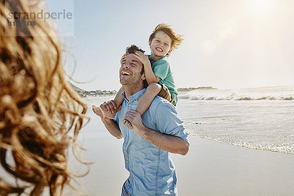 Vater trägt seinen kleinen Sohn auf den Schultern am Strand.