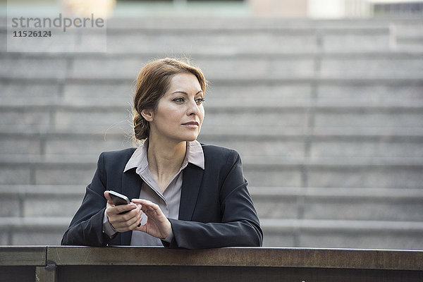 Geschäftsfrau hält Handy im Freien und schaut weg.