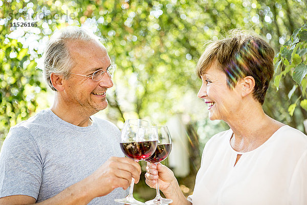 Lächelndes älteres Paar klirrende Rotweingläser im Freien