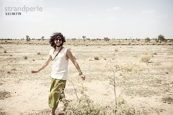 Lächelnder Mann mit Sonnenbrille,  der allein in der Wüste unterwegs ist.
