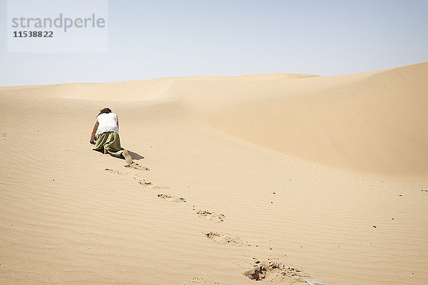Ein Mann,  der allein in der Wüste auf allen Vieren kriecht.